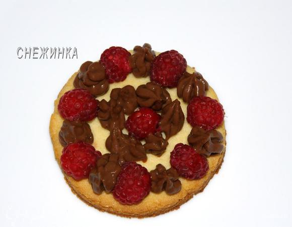 Переходим к сборке. На один миндальный коржик кладем через расстояния по кругу и в центре ягоды малины. Между ними высаживаем с помощью кондитерского мешка или шприца крем.