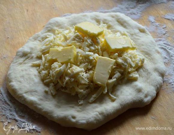 После из каждого шарика руками формируем лепешку, слегка растягивая, в середину каждой кладем тертый сыр (не жалеем) и кусочки сливочного масла..