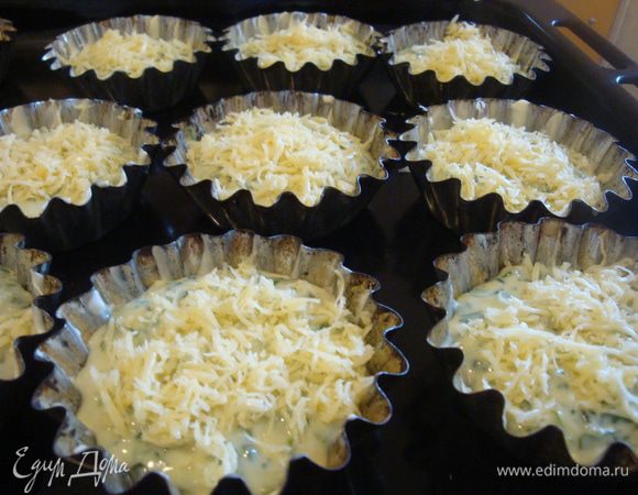 Формочки для кексов смазать оставшимся сливочным маслом, разложить по ним равными порциями тесто. Оно должно заполнить 2/3 объёма формочек. Присыпать оставшимся сыром и запекать в разогретой до 200 градусов духовке 25 минут. 