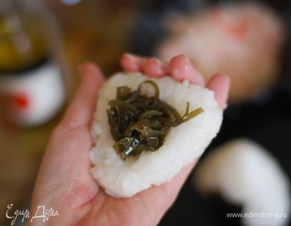 Руки смочите в подсоленной воде, чтобы к ним не прилипал рис. Положите рис в ладонь, слегка сжимая, спрессуйте его и придайте желаемую форму. Двумя пальцами сделайте углубление посередине, в которое положите начинку. Возьмите еще немного риса и «заклейте» углубление. Придайте онигири форму треугольника, переверните колобок несколько раз, после чего оберните его нори (шершавой стороной внутрь).