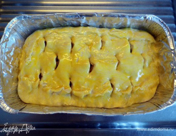 Из большей части теста приготовим пирог с капустой. Делим тесто на две неравные части. Большую раскатаем в пласт, накроем форму для выпечки (у меня алюминиевая 15х25 см) и сформируем дно и бортики. Выложим жареную капусту, равномерно распределим её по форме и накроем пластом теста, раскатанным из маленькой части. Защипим края пирога, смажем его  яичным желтком и кухонными ножницами надрежем в нескольких местах верхушку пирога.