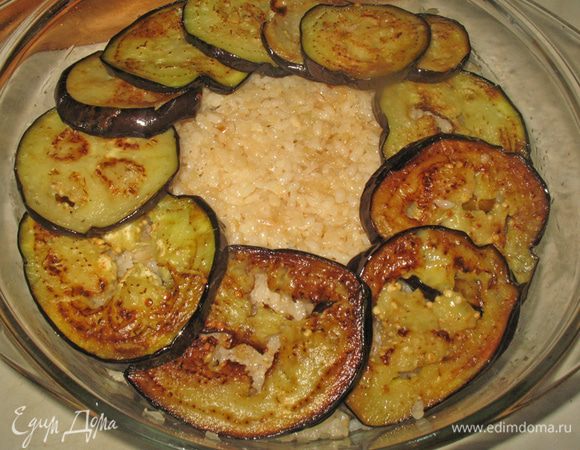 Сверху расстилаем рис, снова баклажаны и сверху ломтики помидор. Каждый слой овощей немного посолить.