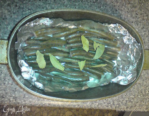 На дно утятницы (или иной посуды с толстым дном) положить 2-3 чайных пакетика и сверху фольгу, затем уложить рыбку брюшками вниз (это важно, чтобы рыбка не превратилась в кашу) в один слой, добавить лавровый лист и перец горошком по вкусу. Уложить следующий слой рыбки, но не больше 2/3 утятницы, иначе масло будет выкипать и гореть.
