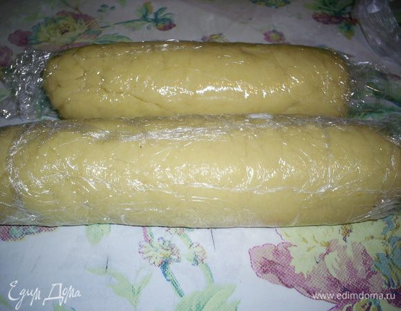 В полученную массу добавляем натертую цедру, стакан муки и соду. Перемешиваем. Затем постепенно всыпая остальную муку, замешиваем крутое тесто. Делим его на две части, каждую раскатываем колбаской, диаметр которой будет равен диаметру нашего будущего печенья. Колбаски заворачиваем в пищевую пленку и отправляем в морозилку.
Если вы не планируете печь печенье сегодня, то смело можете забыть про тесто до нужного случая. Если же печенье планируется сегодня, то часа через два, можно вынимать тесто, оно должно затвердеть, но хорошо резаться ножом.