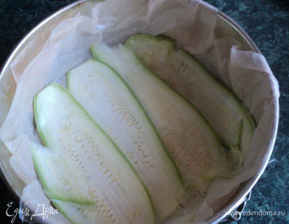 Форму для выпечки (у меня Ф-18 см)  застелить пергаментом. Для того, чтобы пергамент лучше прилегал, можно предварительно смочить его водой. Смазать маслом. На дно выложить внахлест пластинки кабачка.