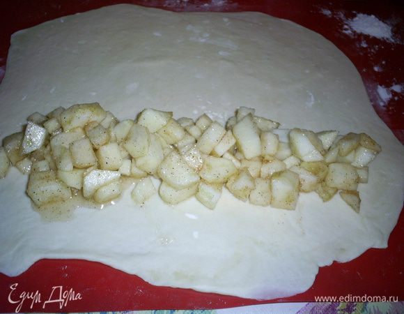 Тесто делим на 5 частей. Каждую раскатываем в тонкий прямоугольный пласт. Тесто по консистенции похоже на пластилин и очень послушное. Рабочую поверхность и тесто лучше припудрить мукой, так будет легче работать.
На широкий край пласта выкладываем яблочную начинку.