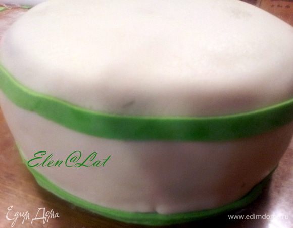 Охлажденный торт, покрыть любым масленым кремом, например, сгущенка и сливочное масло, под мастику. Покрыть белой мастикой. Из зеленой мастики сделать полосочки и украсить ими торт, приклеивая их с помощью капельки воды.