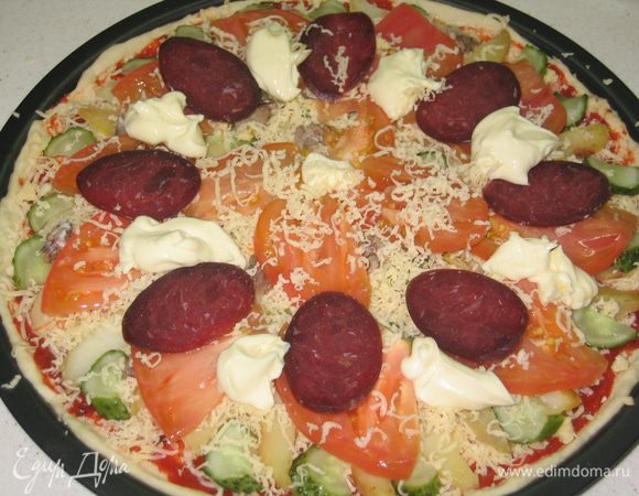 Посыпать сверху сыром (1/2 часть оставшегося количества). Помидор нарезать тонкими пластинками и разложить сверху. также поступить и с колбасой. В промежутки между кусочками колбасы выложить чайной ложкой плавленный сыр