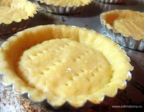 Формочки для тарталеток смазать маслом.
Тесто очень нежное, поэтому аккуратно раскатайте его на припыленной мукой доске тонким слоем, вырезать круги диаметром чуть больше формочек для тарталеток и аккуратно распределите его по формочке (старайтесь как можно меньше трогать его руками). Проколоть тесто вилкой.