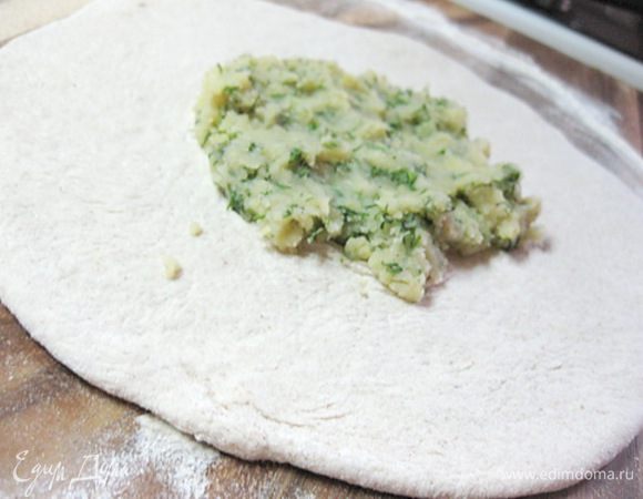 Теперь приступаем к лепке лепешек.
Взять половину теста, раскатать его в небольшую лепешку (не тонко! из этого куска теста получится в итоге большая лепешка по размеру сковороды, а на этом этапе вы должны раскатать ее в два раза меньше).
Положить в центр немного картофельной смеси.