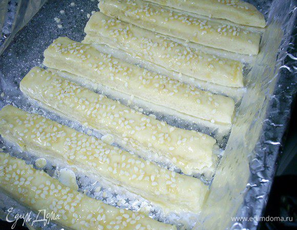 После последнего складывания теста в конверт, раскатываем его в пласт толщиной чуть больше сантиметра. Разрезаем его на полоски шириной сантиметр. Длину будущих палочек выбираете сами. Заготовки будущих палочек перекладываем на противень смазанный маслом или застеленный пергаментом. (У меня противень застеленный фольгой и смазанный маслом). Смазываем их сверху взбитым яйцом и посыпаем кунжутом и слегка солью (с солью не перестарайтесь).