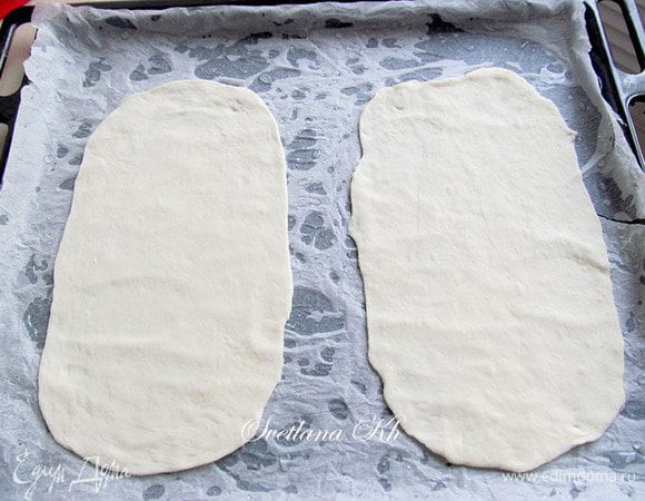 Затем каждый колобок тонко раскатайте. Форма должна быть круглой, но я сделала продолговатую, чтобы на противень помещалось 2 шт.