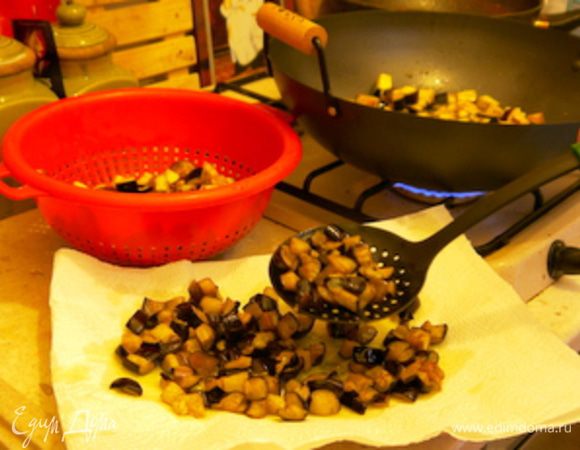 Обжарить баклажаны на большом количестве оливкового масла. Достать шумовкой из масла и перенести на блюдо, накрытое бумажными полотенцами, чтобы они впитали излишек масла.