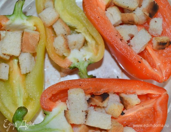 Перцы уложить в стеклянную форму для выпечки. Заполнить их сухариками. 