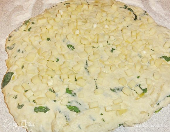 Тесто увеличится 2-2,5 раза. Выложите тесто на стол посыпанный  мукой и придайте тесту форму лепешки руками. Нарежьте сыр мелкими кубиками. Распределите сыр на поверхности теста.