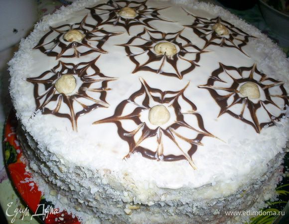 Бока торта обсыпаем смесью измельченных обрезков и кокосовой стружки. Шоколад растапливаем с 1 чайной ложкой сметаны, наполняем корнетик и рисуем по два концентрических круга. Затем зубочисткой делаем паутинку., в центр каждой кладем по орешку. Отправляем торт в холодильник, желательно на ночь.  Приятного аппетита!