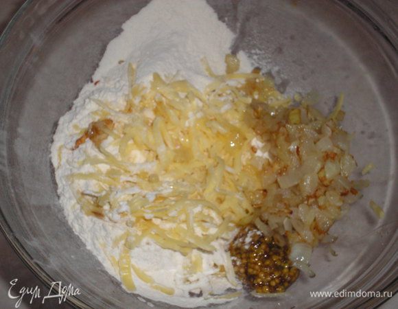 Лук нарезаем кубиком и обжариваем до золотистого цвета на растительном масле. Сыр натираем на крупной терке, добавляем мягкое сливочное масло, горчицу, муку, разрыхлитель, перец, соль. 