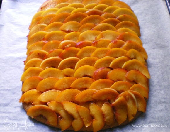 На пирог черепицей разложить ломтики персиков.