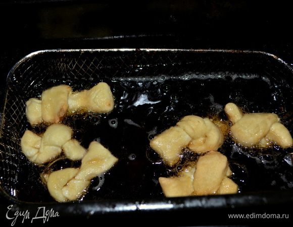 Подготовим фритюрницу с маслом или жаровню. А также тарелку с бумажным полотенцем. Фритюрницу разогреваем до 180°C. Каждую полоску сворачиваем в свободный узел. Выкладываем во фритюрницу порционно по 5–6 узелков. Обжариваем по 2 минуты примерно или до золотистого цвета. Готовые узелки выкладываем на тарелку с бумаж. полотенцем.