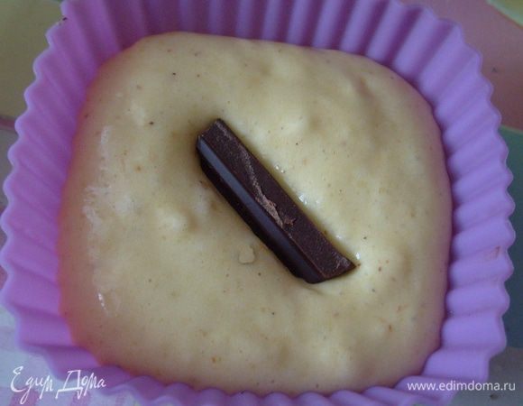 Выложить тесто в формочки, заполняя их примерно на 2/3. В центр каждой формочки положить кусочек шоколада, немного "втаптывая" его в тесто.