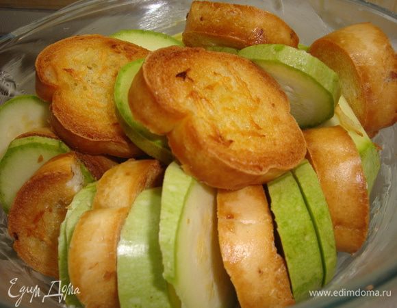 Выложить ломтики кабачков и хлеба слоями в смазанную жиром форму. Залить сырным соусом. Посыпать сверху тертым сыром и запекать окло 35 минут. Подавать на стол, украсив базиликом!