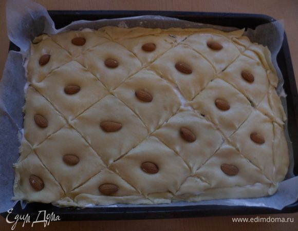 Накрыть вторым пластом теста и выложить оставшуюся начинку, и наконец накрыть третьим пластом теста (начинки на ней не должно быть). Надрезать верхний слой теста на ромбики и в каждый ромбик вложить  миндаль. Сверху пирог смазать взбитым желтком. Поставить готовый пирог в разогретую до 180 градусов духовку и выпекать 45-50 минут. 
