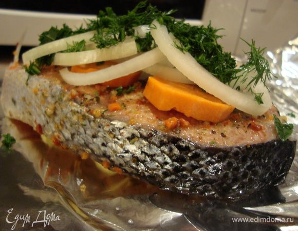 На двойной лист фольги «HomeQueen» положить 1-2 ломтика (1 ч.л.) сливочного масла на него выложить предварительно пропитанный стейк лосося, кружочки моркови, лук кольцами и измельченную зелень укропа.