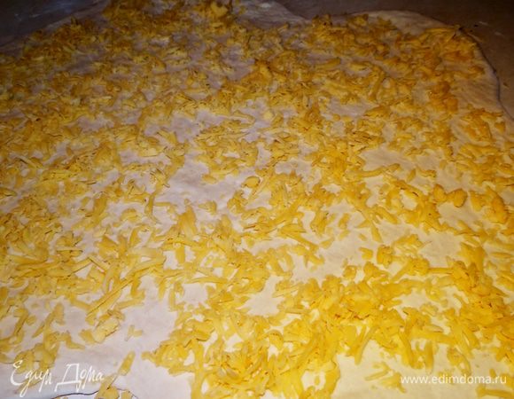 Тесто раскатать в прямоугольный пласт, сверху равномерно пересыпать сыром..