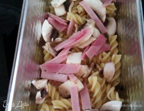 Слегка смазываем форму оливковым маслом. Выкладываем слой из половины фузилли, половины грибов и ветчины.