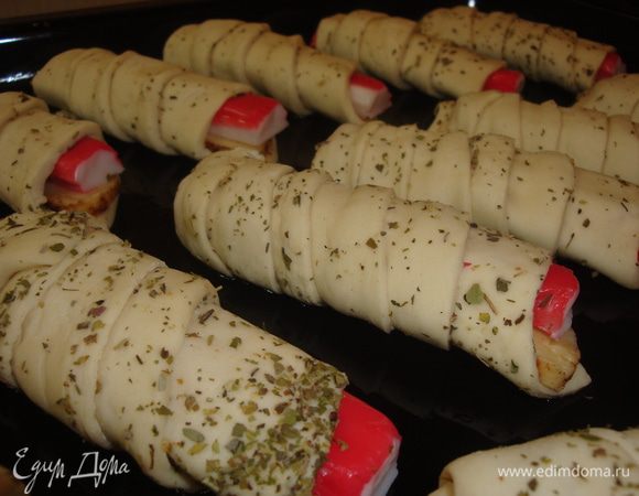 Противень смазать растит. маслом. На крабовую палочку положить кусочек сыра, затем обматываем все слоеным тестом, свернув в рулетик. Завитушки выложить на противень. Духовку разогреть до 180 градусов и выпекать завитушки в течении 25-30 минут, пока они не зарумянятся. Затем немного остудить и подавать на стол. Украсить по желанию.