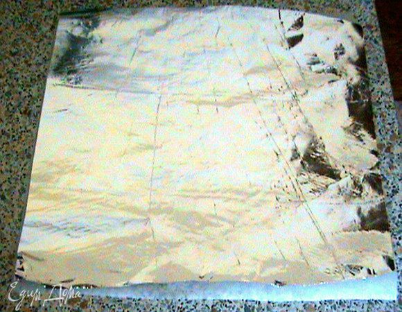 Вырезаем из бумаги для выпечки большой квадрат. Такой же вырезаем из фольги и кладём на бумажный (этим квадратом мы будем запаковывать форму). Проверьте, чтобы квадраты были на 5-6 см больше диаметра формы.