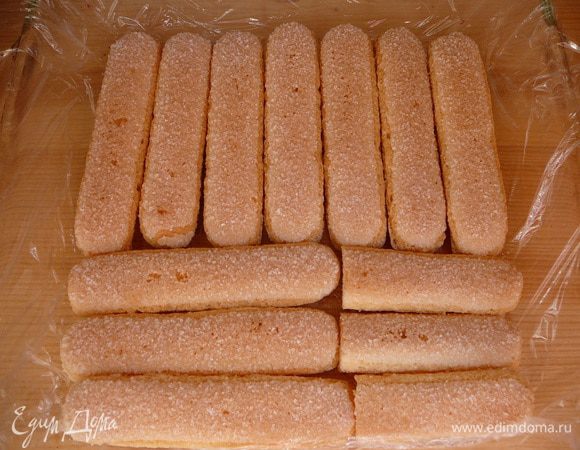 Форму выстелить пищевой пленкой, выложить слой бисквитного печенья.