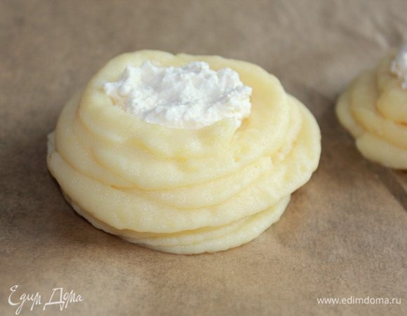 В центре каждой ватрушки сделать небольшое углубление и выложить творожную начинку. В миске разбить яйцо, взбить и смазать каждую ватрушку. 