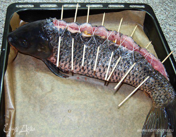 Сколоть отверстие деревянными шпажками. Будьте осторожны! Рыбка будет сопротивляться, поэтому можете сделать как мы: острым тонким ножом слегка подрезать шкуру и только потом вставить шпажки. Стянуть разрез кулинарной нитью (как шнурок в ботинках).
Развести 1 ч.л. крахмала в 3 ст.л. воды и обмазать этой смесью рыбу.  Выложить карпа на противень, застеленный пергаментом. Готовить в разогретой до 180 гр. духовке 25 минут.
