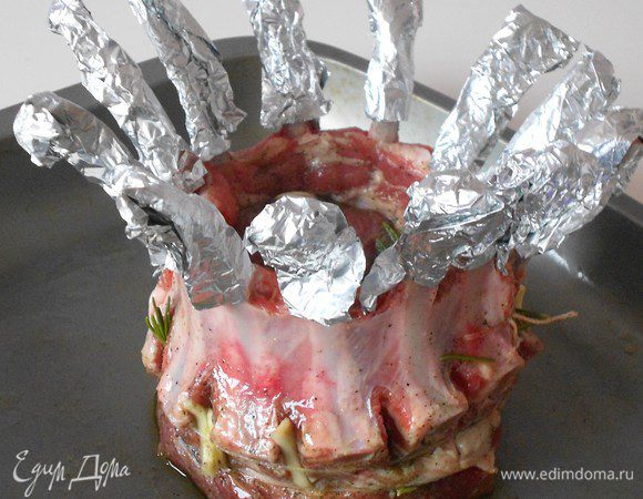 Сопоставить оба каре так, чтобы напоминало корону.Кулинарным шпагатом с помощью большой иглы подтянуть края плотно друг к другу, захватывая крайние косточки.Ниже косточек обвяжите мякоть шпагатом, это поможет удержать круглую форму блюда. Натрите смесью соли,перца и розмарина,Вложите кусочки чеснока в разрезы и заправьте под шпагат.Перенесите мясо на противень и смажьте маслом.Косточки оберните фольгой от "HQC", иначе они обгорят.