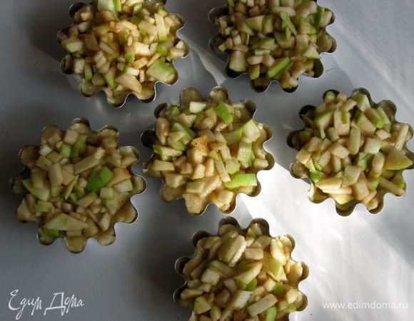 Охлажденное тесто равномерно распределить по дну и бортикам формочек, разложить сверху яблоки и выпекать 15 минут при температуре 180 градусов.