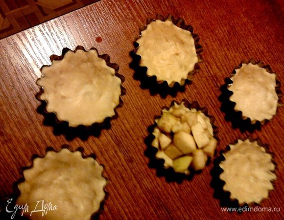 Охлажденное тесто разложить по формочкам, равномерно распределив по дну и бортикам.
Выложить яблоки в формочки с тестом и поставить в разогретую духовку на 12–15 минут.