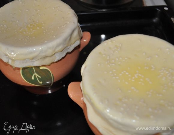 Взбить желток и смазать им горловины горшочков. Накрыть горшочки кругами теста, хорошо прижать по краям. Смазать «крышечки» оставшимся желтком и посыпать кунжутом. 
Поставить в духовку, разогретую до 200 градусов. 
Держать там до готовности теста,примерно 20 минут.