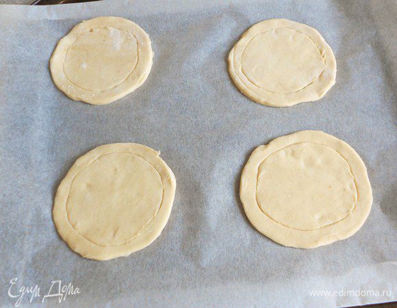  Положить на присыпанную мукой поверхность тесто и, используя маленькую миску или блюдце как шаблон, вырезать 4 круга по 10 см в диаметре. Переложить их на противень, застеленный бумагой для выпечки от "HQC". Острым ножом сделать круговые неглубокие надрезы в дисках, отступив 1 см от края. Не прорезать слой теста насквозь до бумаги!