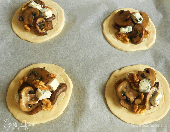 Смешать грецкие орехи, кусочки сыра с грибами и ложкой выложить начинку в середину каждого круга. Кистью смазать края взбитым яйцом.