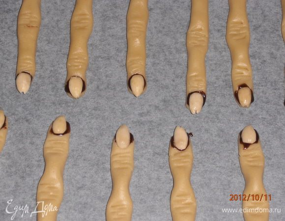 Отщипните маленькие кусочки, придайте форму пальца и ножом сделайте полоски на сгибах. Шоколад растопите, смешайте с водой и нанесите на концы в местах «ногтя». Сверху положите миндаль. Выпекайте при 180 °С 20 минут.