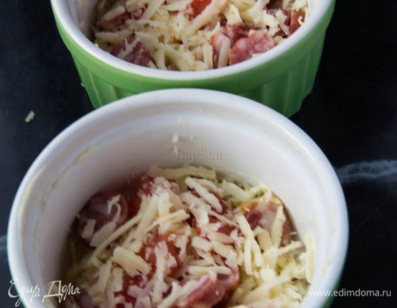 В каждую кокотницу распределить натертый сыр, нарезанные кольцами колбаски и томаты, очищенные от кожицы и нарезанные кубиками.