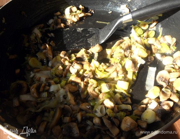 В сковороде разогреть немного оливкового/растительного масла, обжарить лук-порей (нежную часть), минут 10, не давая потемнеть. Присоединить тонко порезанные шампиньоны и готовить еще 10 минут, или до желаемого состояния грибов. 