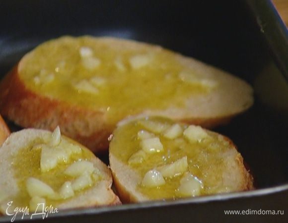 Багет нарезать ломтиками наискосок, выложить в небольшой противень и полить половиной растопленного масла с чесноком. Отправить гренки в разогретую духовку на 10 минут.