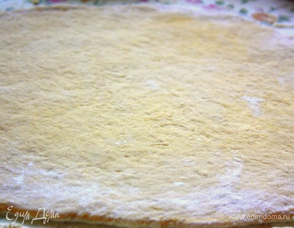 Выложить тесто на коврик, припыленный мукой. Руками распределить в прямоугольник.