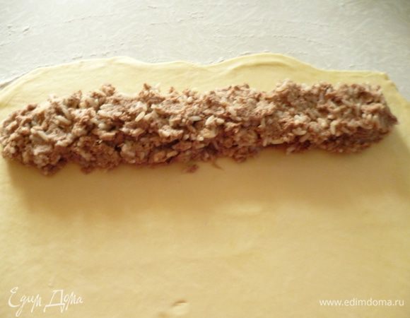 Достаем одну часть теста из холодильника,стол подпылить мукой и раскатать тоненький корж (как на пельмени) шириной 20 см и длиной 30-35 см. Немного отступив от края выкладываем начинку толстой колбаской по всей длине коржа.Я иногда делаю два длинных рулета,а иногда три поменьше длиной.