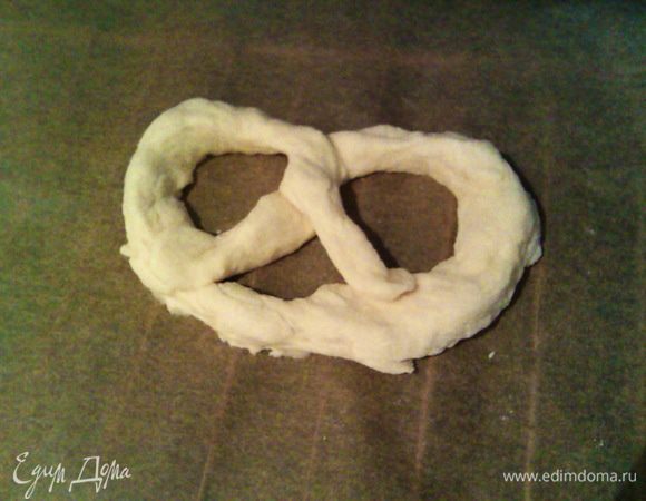 Быстро перекручиваем кончики между собой и приклеиваем концами к основе, перекладывая на противень. Подправляем их форму двумя руками, поставив 2 больших пальца в основание брецеля, а остальные в верхние дырочки, слегка растягивая.