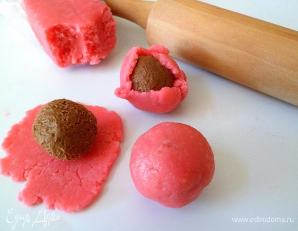 Берем марципановую массу и также делим на равные части, расплющиваем при помощи пальцев. Затем застывшие шарики с нугой и орехами одеваем в марципан, аккуратно скатав в шары.