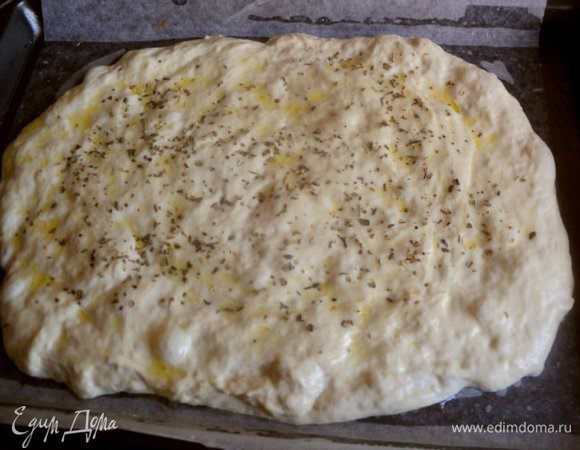 Противень застелить бумагой для выпечки, смазать маслом. Выложить тесто, разровнять смоченными маслом руками в пласт толщиной 1-1.5 см. Смазать сверху оливковым маслом, посыпать сушеным орегано.