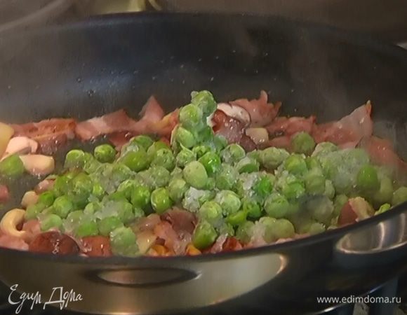Когда бекон обжарится до золотистого цвета, снять сковороду с огня, добавить замороженный зеленый горошек и перемешать.